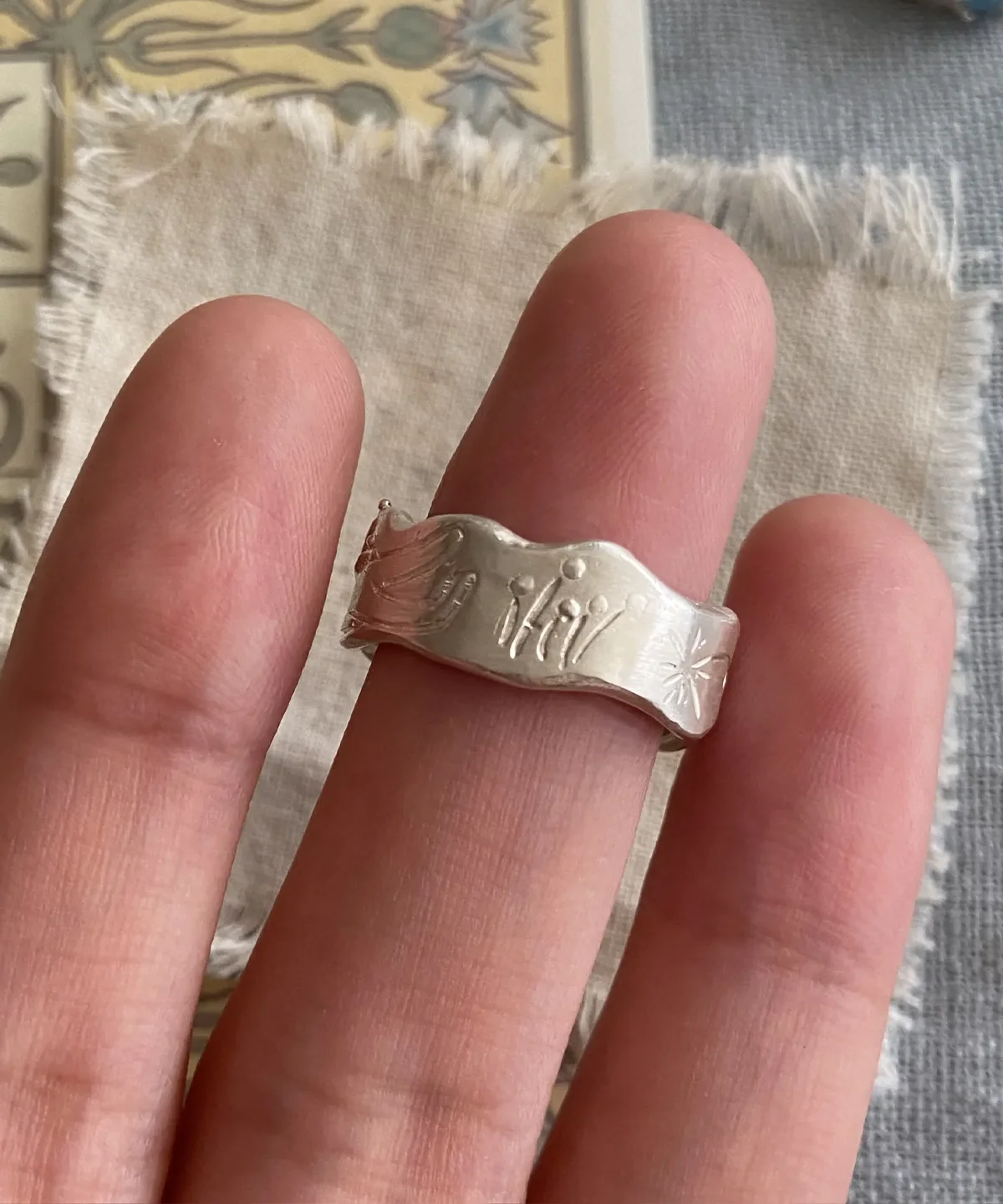 Hand wearing a Handmade 999 Silver Ring with engraved butterfly, floral, and sunburst motifs, featuring a light blue Aquamarine gemstone; a poetic Aquamarine Ring crafted in fine silver, celebrating March birthstone elegance and nature-inspired artistry.