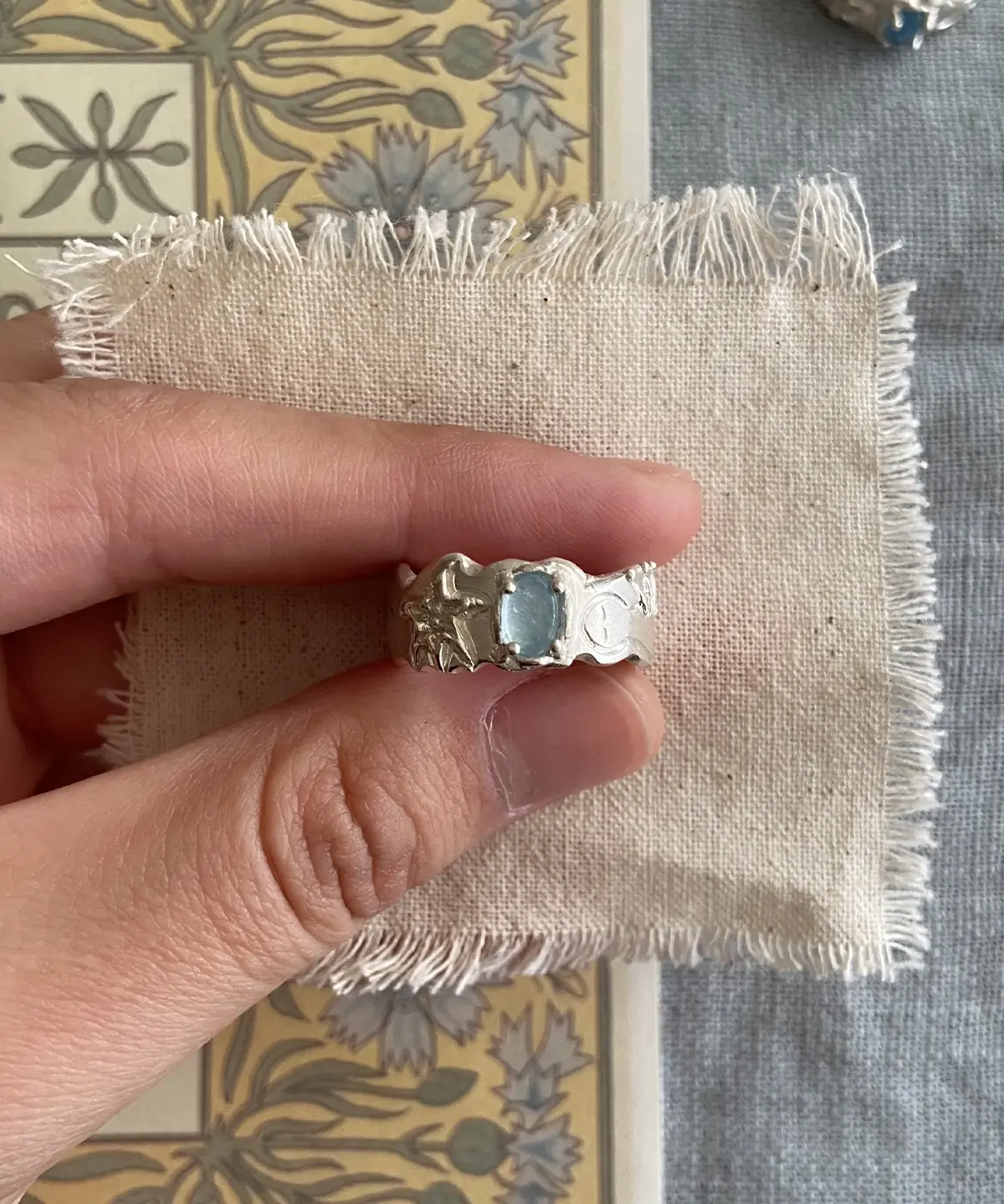 Hand holding a Handmade 999 Silver Ring with light blue Aquamarine gemstone, engraved star and circular motifs; a poetic Aquamarine Ring crafted in fine silver, celebrating March birthstone elegance and artisan detail.