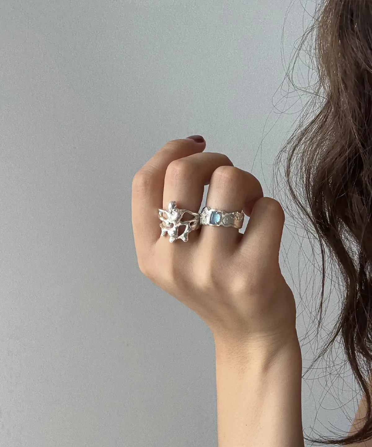 Close-up of a hand wearing two silver rings, one with a rectangular Aquamarine gemstone and one with an abstract coral-like design; Handmade 999 Silver Ring showcasing artistic texture and celebrating the March birthstone with Aquamarine Ring elegance.