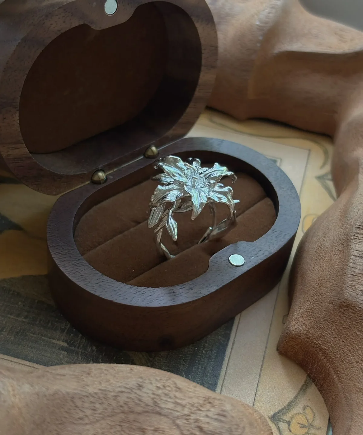 Handmade S925 Sterling Silver Lily Ring with intricate floral design, placed in an open wooden ring box; detailed petals and leaves evoke natural elegance, highlighting the craftsmanship of this artistic Silver Ring inspired by the lily flower.