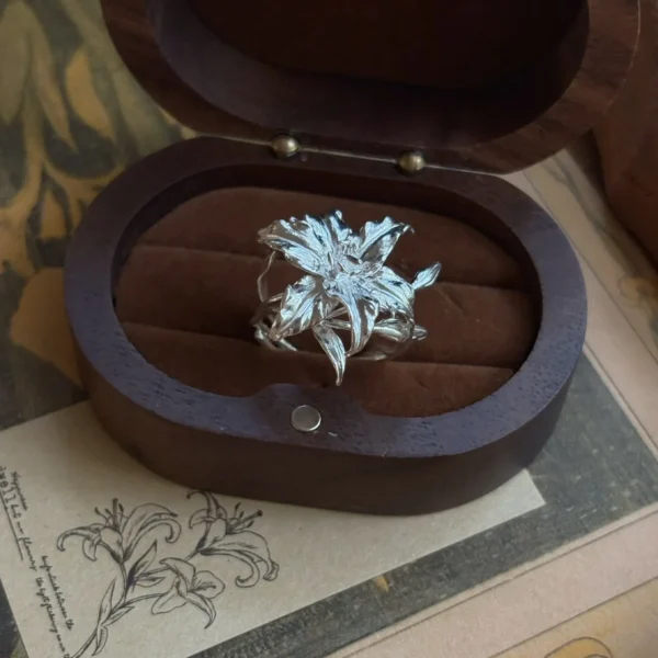 Handmade S925 Sterling Silver Lily Ring with sculpted petals and leaves, placed in a dark wooden box with soft interior; a nature-inspired Silver Ring celebrating the elegance and symbolism of the lily flower in detailed craftsmanship.