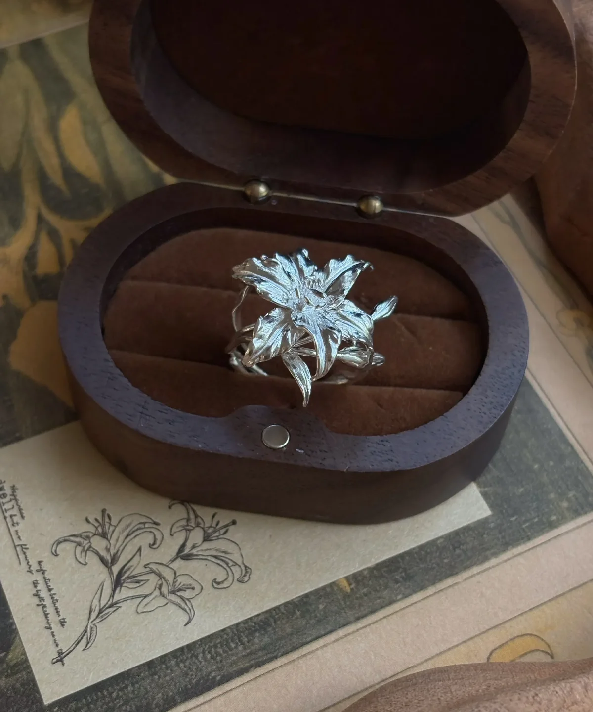 Handmade S925 Sterling Silver Lily Ring 03 Handmade S925 Sterling Silver Lily Ring with sculpted petals and leaves, placed in a dark wooden box with soft interior; a nature-inspired Silver Ring celebrating the elegance and symbolism of the lily flower in detailed craftsmanship.