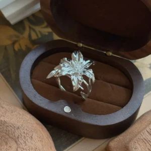 Handmade S925 Sterling Silver Lily Ring with sculpted petals and lifelike floral textures, placed in an open wooden box with soft brown interior; a botanical Silver Ring inspired by the elegance of the lily flower.