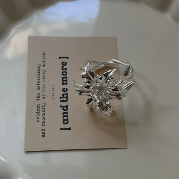 Handmade S925 Sterling Silver Lily Ring with sculpted petals and vine-textured band, placed on a beige card in a ceramic dish; a botanical Silver Ring inspired by the lily flower’s elegance and crafted with artisanal detail.