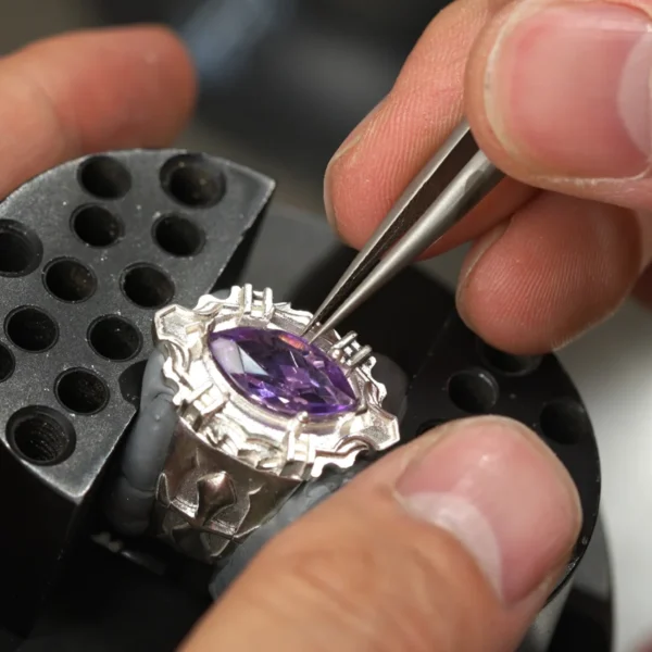 Katekyo Hitman Reborn! Vongola Ring-Handmade in Sterling Silver 04 Close-up of a jeweler setting a marquise-cut purple gemstone into a Custom Vongola Silver Ring using precision tweezers; the ring is secured in a clamp, highlighting the craftsmanship and detail of this Handmade Custom Ring in Sterling Silver.