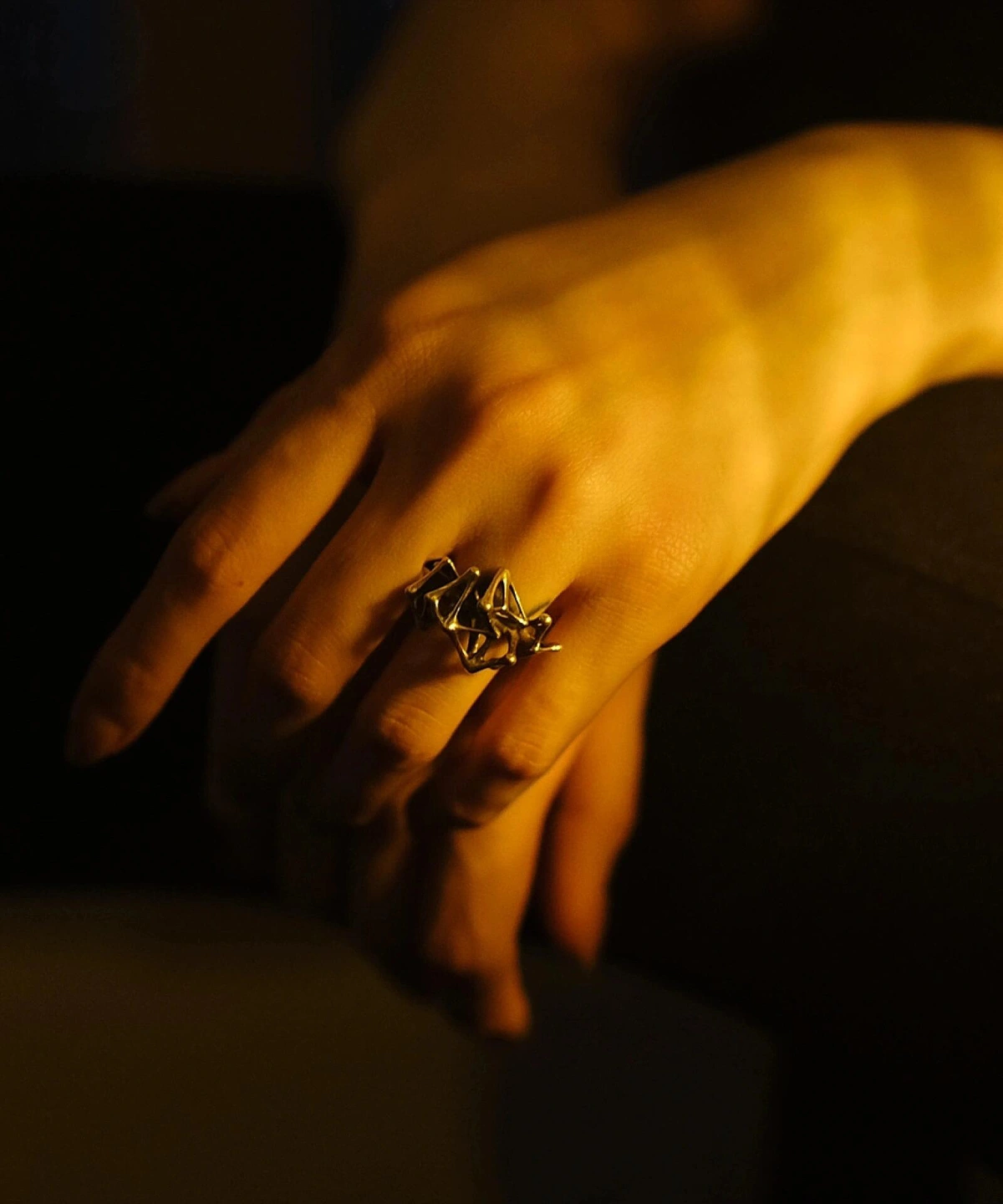 Leaping Orbit Handcrafted 999 Fine Silver Statement Ring with angular geometric design, worn on hand; a bold Silver Statement Ring featuring sculptural interlocking shapes, highlighted by warm dramatic lighting.