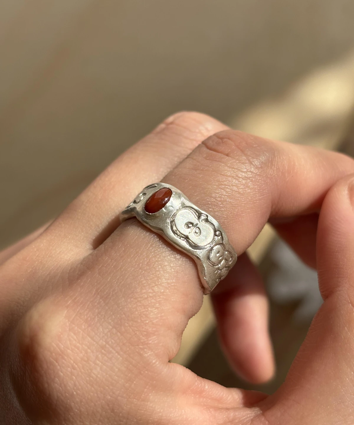 South Red Agate Ring in 999 Silver featuring a reddish-brown oval gemstone and engraved cartoon-style apple faces; a handcrafted 999 Silver Ring with whimsical texture and symbolic fruit-inspired design, worn on hand in close-up view.