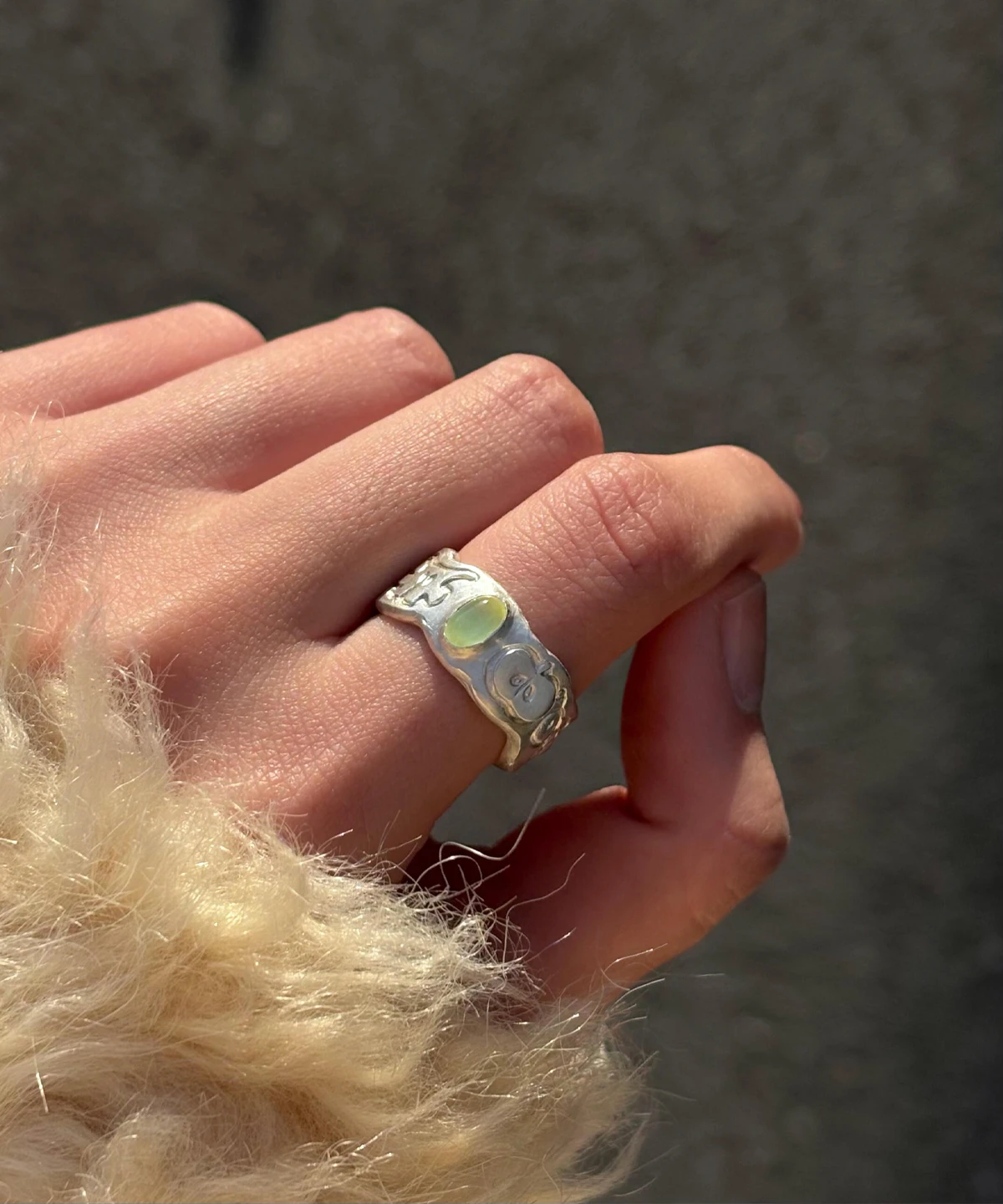 Natural Peridot Ring in 999 Silver featuring light green oval gemstone and engraved apple-inspired face motifs; a handcrafted 999 Silver Ring with organic curves and textured surface, worn on hand against soft fabric.