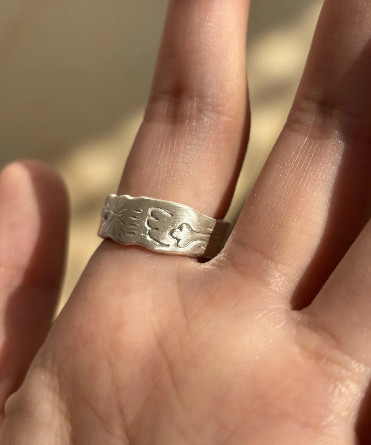 Natural Peridot Ring in 999 Silver with light green oval gemstone and engraved motifs including paw print, bone, and sunburst; a handcrafted 999 Silver Ring with matte finish and symbolic animal-inspired design, worn on hand in close-up view.