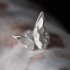 Close-up of a handcrafted S925 Sterling Silver Butterfly Ring with intricate wing details and polished finish, placed on soft textured skin; elegant Silver Ring design showcasing delicate craftsmanship and nature-inspired beauty.