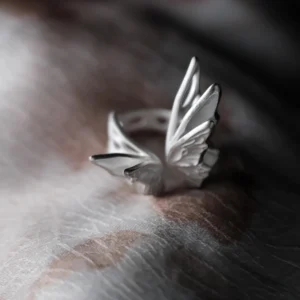 Close-up of intricately designed S925 Sterling Silver Butterfly Rings with sculptural wings and blue gemstones, arranged on a dark textured surface with decorative beads; elegant Silver Ring collection showcasing nature-inspired artistry.