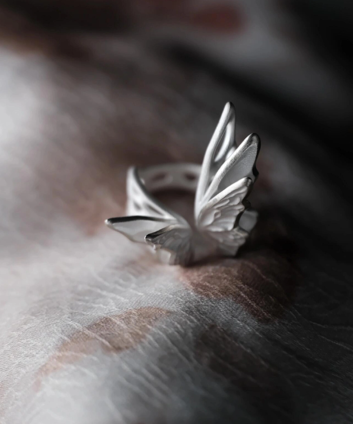 Close-up of intricately designed S925 Sterling Silver Butterfly Rings with sculptural wings and blue gemstones, arranged on a dark textured surface with decorative beads; elegant Silver Ring collection showcasing nature-inspired artistry.