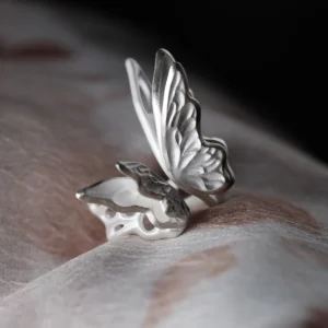 Close-up of a handcrafted S925 Sterling Silver Butterfly Ring with etched wing details, resting on soft fabric; elegant Silver Ring design showcasing delicate craftsmanship and nature-inspired beauty in a sculptural Butterfly Ring form.