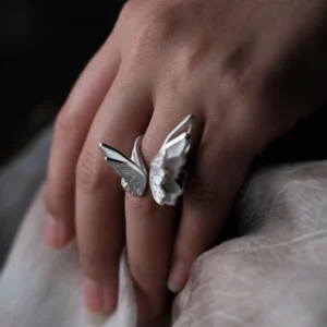Close-up of a hand wearing a S925 Sterling Silver Butterfly Ring with sculptural open-wing design, resting on soft fabric; elegant Silver Ring showcasing lifelike contours and handcrafted Butterfly Ring artistry inspired by nature.