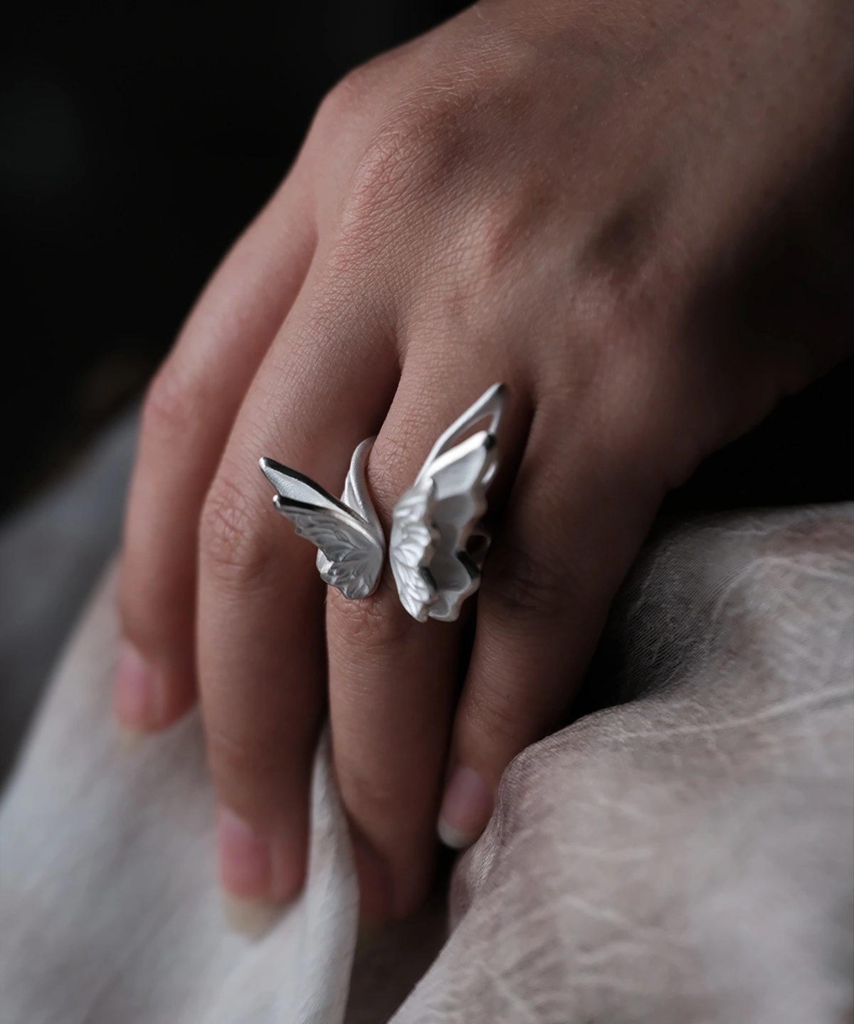 Close-up of a hand wearing a S925 Sterling Silver Butterfly Ring with sculptural open-wing design, resting on soft fabric; elegant Silver Ring showcasing lifelike contours and handcrafted Butterfly Ring artistry inspired by nature.
