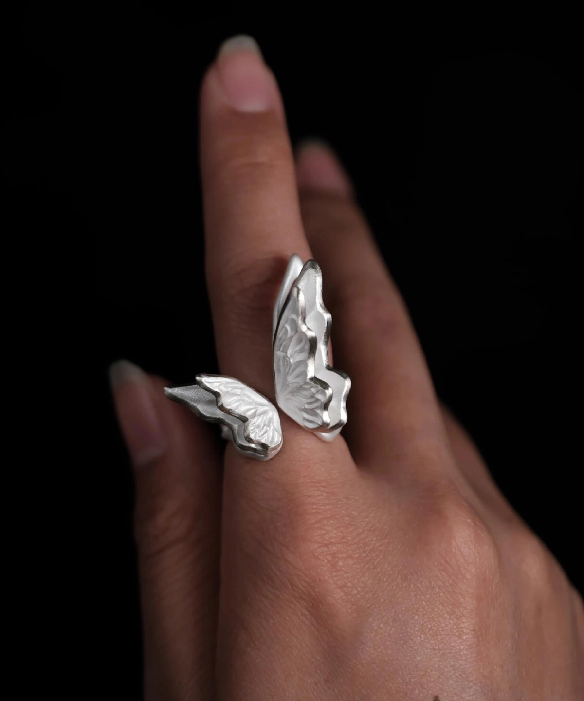 Close-up of a hand wearing a S925 Sterling Silver Butterfly Ring with sculptural open-wing design and lifelike texture, set against a black background; elegant Silver Ring showcasing handcrafted detail and nature-inspired Butterfly Ring artistry.