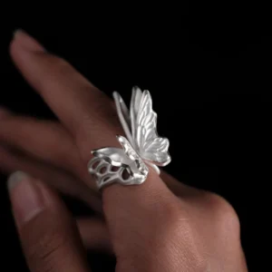 Close-up of a hand wearing a S925 Sterling Silver Butterfly Ring with raised wings and sculptural texture, set against a dark background; elegant Silver Ring design showcasing handcrafted Butterfly Ring artistry and lifelike wing detail.