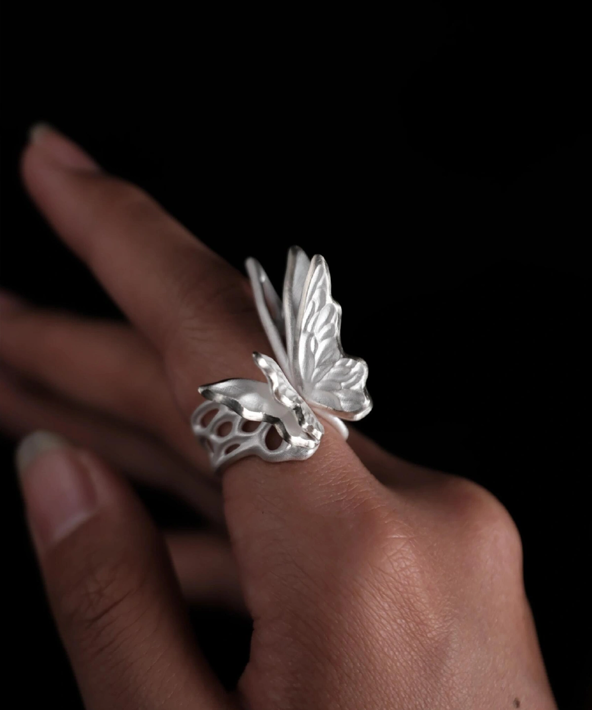 Close-up of a hand wearing a S925 Sterling Silver Butterfly Ring with raised wings and sculptural texture, set against a dark background; elegant Silver Ring design showcasing handcrafted Butterfly Ring artistry and lifelike wing detail.