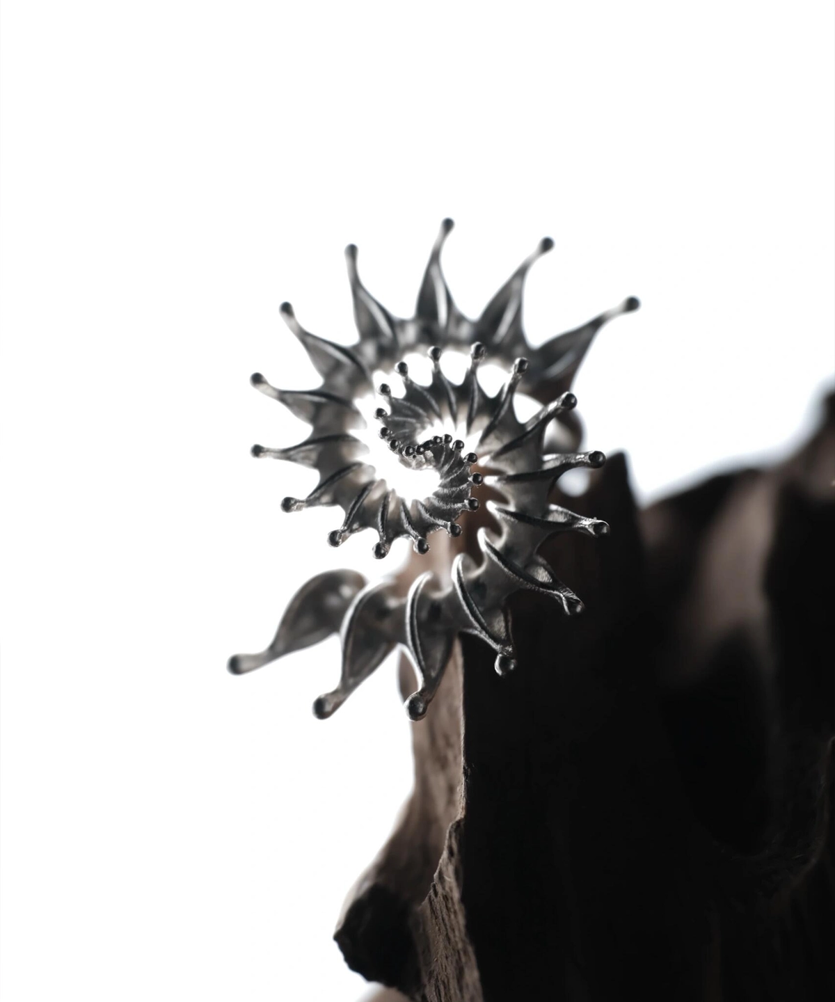 S925 Sterling Silver Spiral Ring Jewelry-Handmade Artistic Statement Ring 04 Close-up of a metallic S925 Sterling Silver Spiral Ring Jewelry with radiating petal-like extensions in a stylized sunburst design, mounted on a dark textured surface; bold Statement Ring showcasing sculptural elegance and intricate Silver Ring craftsmanship.