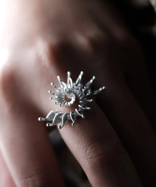 Close-up of a hand wearing a S925 Sterling Silver Spiral Ring Jewelry with radiating petal-like extensions in a stylized sunburst design; bold Statement Ring showcasing intricate craftsmanship and sculptural Silver Ring elegance.