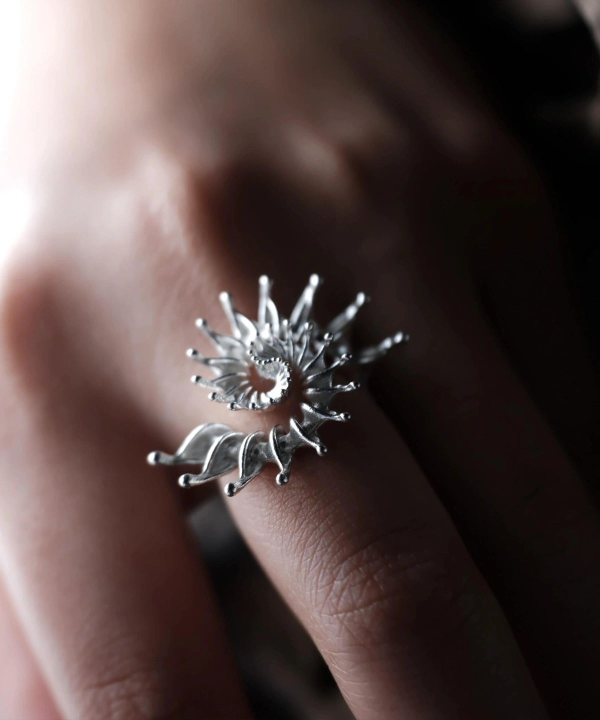 Close-up of a hand wearing a S925 Sterling Silver Spiral Ring Jewelry with radiating petal-like extensions in a stylized sunburst design; bold Statement Ring showcasing intricate craftsmanship and sculptural Silver Ring elegance.