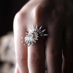 Close-up of a hand wearing a S925 Sterling Silver Spiral Ring Jewelry with radiating sculptural design, resembling a sunburst or nautilus shell; bold Statement Ring showcasing artistic craftsmanship and elegant Silver Ring texture.