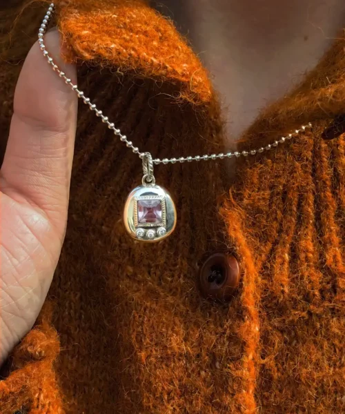 Tamagotchi Necklace with light purple square gemstone and three clear accent stones in S925 silver; held by hands over rust-colored knit fabric, showcasing Pet Necklace craftsmanship and nostalgic charm.