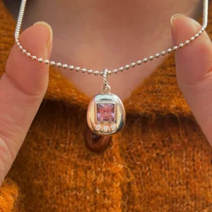 Custom Handmade S925 Sterling Silver Tamagotchi Necklace 002 Tamagotchi Necklace with light purple gemstone and three clear accent stones in S925 silver; held by hands over rust-colored fabric, showcasing Pet Necklace craftsmanship and nostalgic elegance.