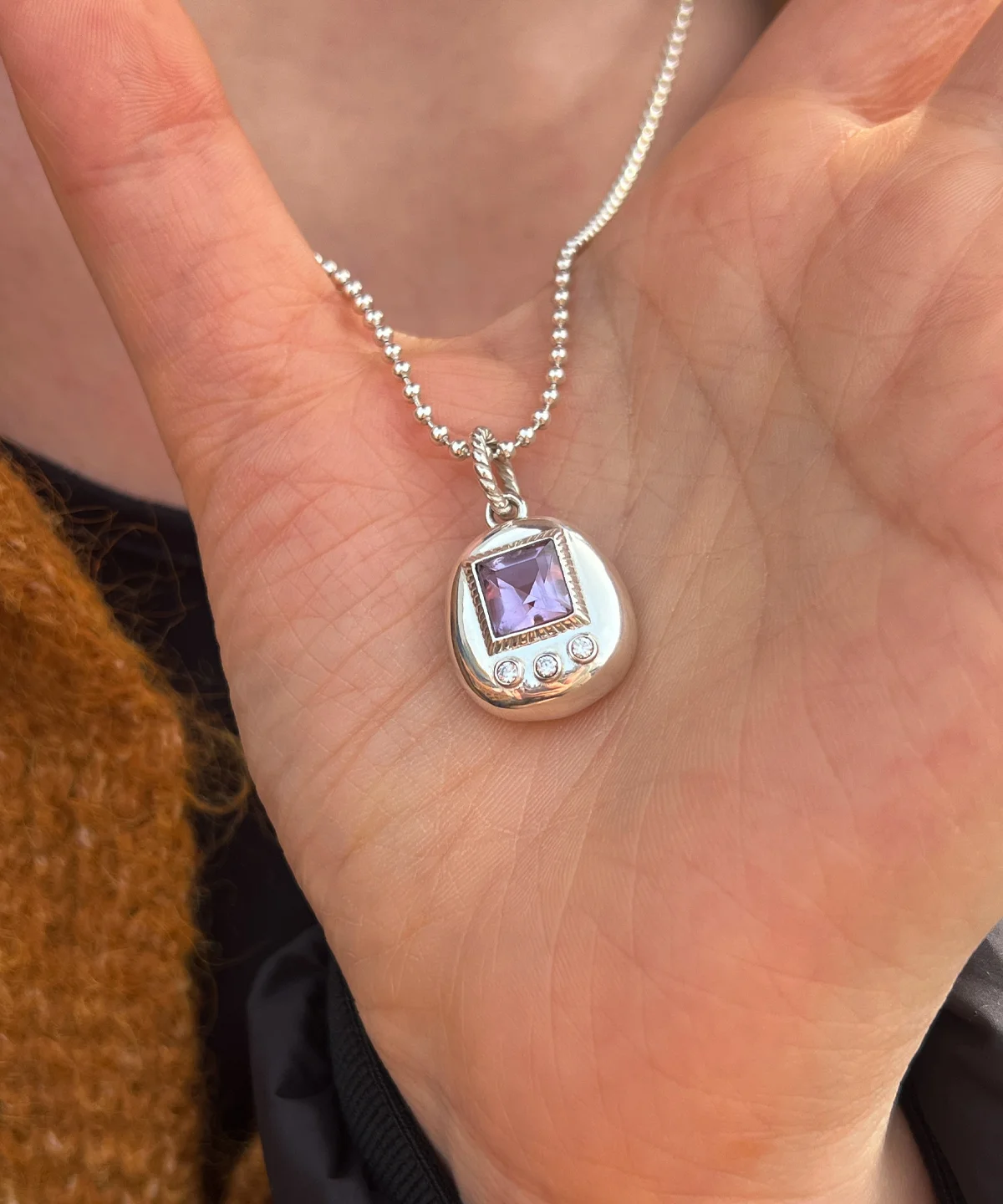 Custom Handmade S925 Sterling Silver Tamagotchi Necklace 03 Tamagotchi Necklace with light purple square gemstone and three clear accent stones in S925 silver, held by hand.
