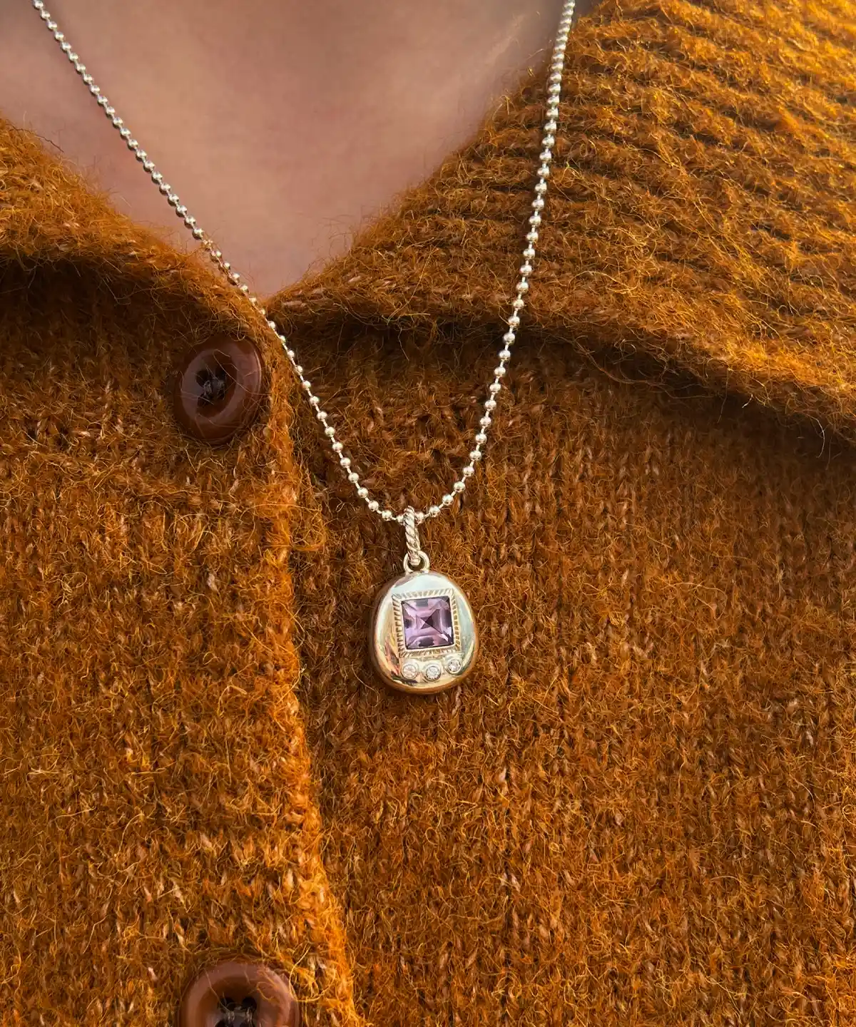Custom Handmade S925 Sterling Silver Tamagotchi Necklace 05 Tamagotchi Necklace with light purple square gemstone and three clear accent stones in S925 silver; worn over brownish-orange knit sweater with buttons, showcasing Pet Necklace elegance.