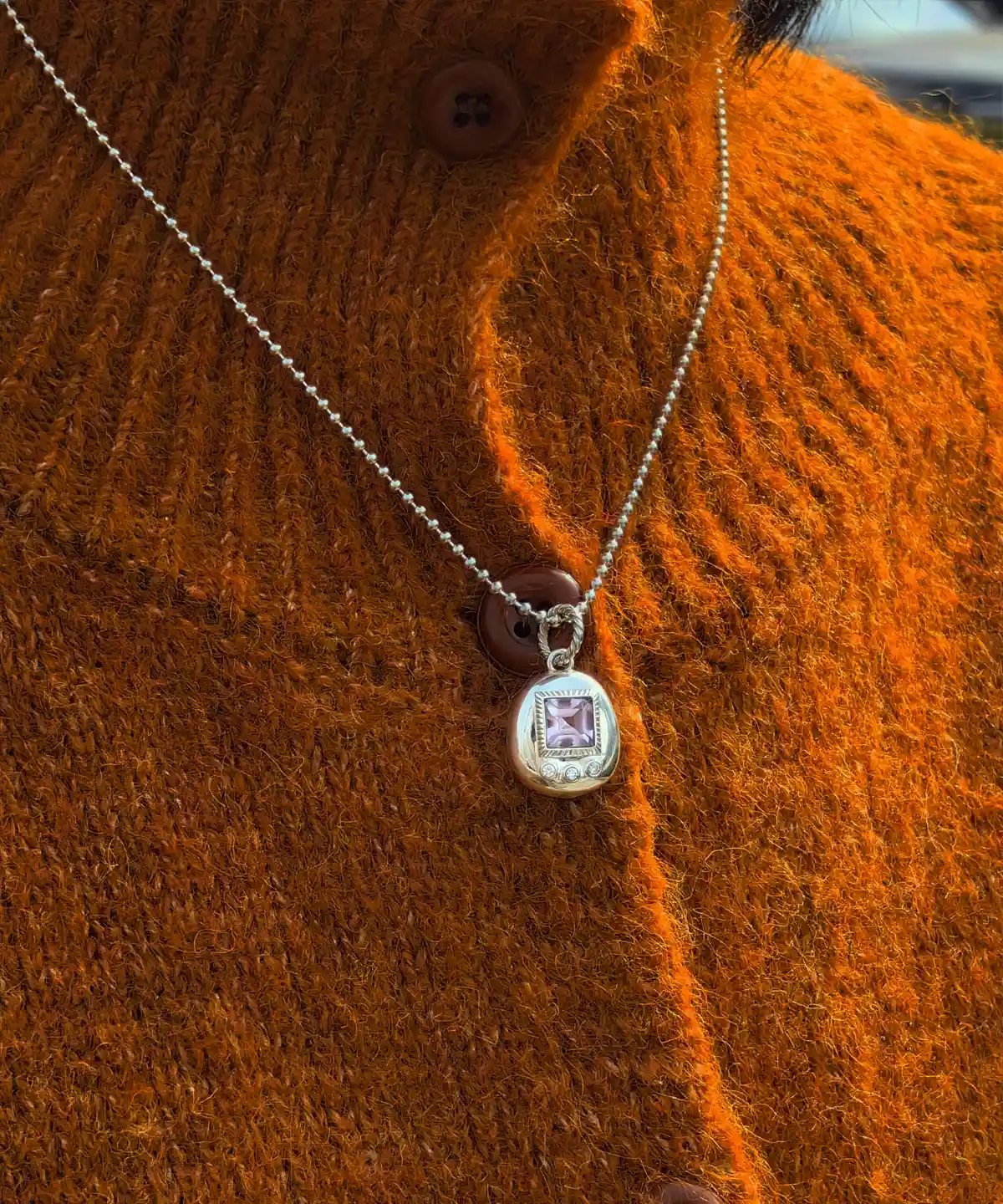 Custom Handmade S925 Sterling Silver Tamagotchi Necklace 06 Tamagotchi Necklace with light purple square gemstone and three clear accent stones in S925 silver; worn over rust-colored knit sweater with buttons, showcasing Pet Necklace elegance and handcrafted detail.