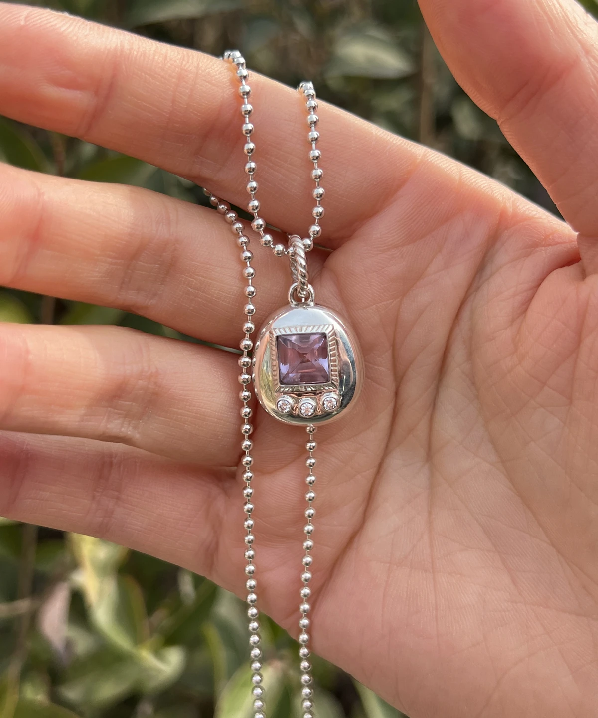 Custom Handmade S925 Sterling Silver Tamagotchi Necklace 08 Tamagotchi Necklace with light purple square gemstone and three clear accent stones in S925 silver; held by hand outdoors with green foliage background, showcasing Pet Necklace craftsmanship and nostalgic charm.