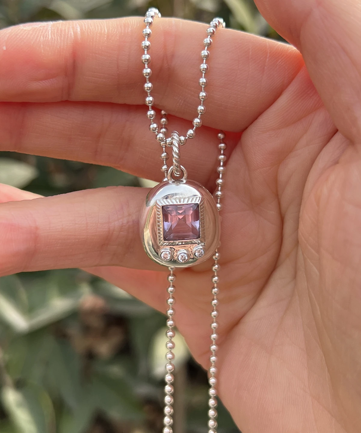 Custom Handmade S925 Sterling Silver Tamagotchi Necklace 09 Tamagotchi Necklace with light purple square gemstone and three clear accent stones in S925 silver; held by hand outdoors with green background, showcasing Pet Necklace craftsmanship and nostalgic charm.