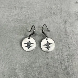 Disc Earrings in S925 Sterling Silver with engraved starburst cutout filled with dark glitter; placed on textured gray surface to highlight handcrafted detail, sparkle contrast, and minimalist elegance in engraved earrings.