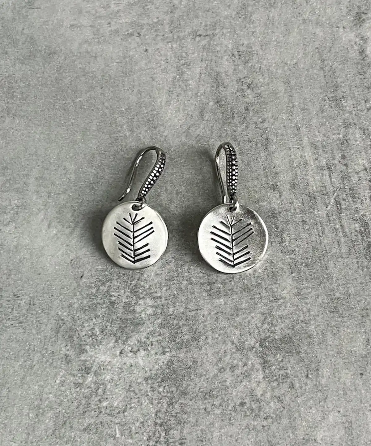 Disc Earrings in S925 Sterling Silver with engraved leaf or branch design; placed on textured gray surface to highlight minimalist elegance, handcrafted detail, and organic artistry in engraved earrings.