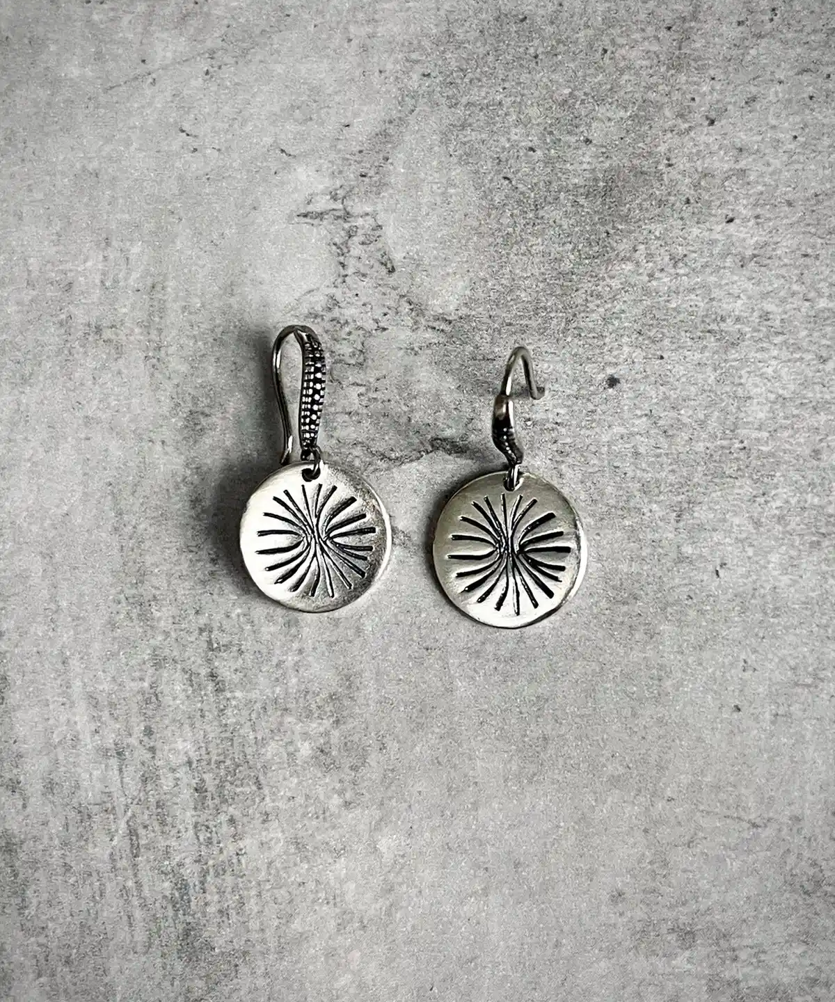 Disc Earrings in S925 Sterling Silver with engraved sunburst design; placed on textured gray surface to highlight handcrafted detail, minimalist elegance, and the radiant etching of engraved earrings.
