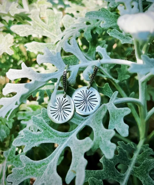 Disc Earrings in S925 Sterling Silver with engraved sunburst design; styled on leafy plant with silvery foliage to highlight handcrafted detail, organic elegance, and the radiant texture of engraved earrings.