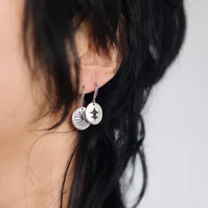 Disc Earrings in S925 Sterling Silver with engraved sunburst and star motifs; worn on ear with dark hair, styled against neutral background to highlight handcrafted detail and artistic symbolism in engraved earrings.