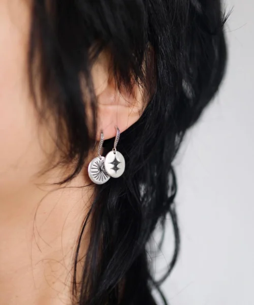 Disc Earrings in S925 Sterling Silver with engraved sunburst and star motifs; worn on ear with dark hair, styled against neutral background to highlight handcrafted detail and artistic symbolism in engraved earrings.