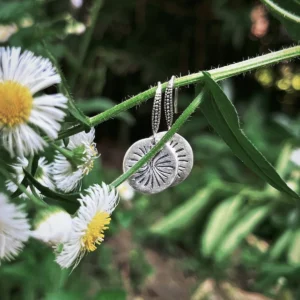 Disc Earrings in S925 Sterling Silver with engraved sunburst design; styled on green plant stem among white daisy flowers, highlighting handcrafted detail and nature-inspired elegance in engraved earrings.