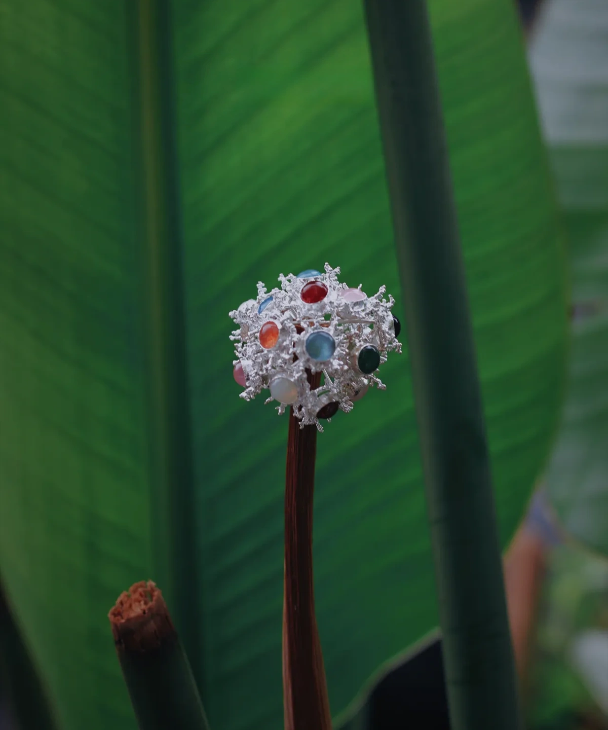 Gemstone Stud Earrings in S925 Sterling Silver with organic splash-inspired design and multicolored stones; decorative piece mounted on plant stem, styled against lush green leaves for vibrant contrast and natural elegance.