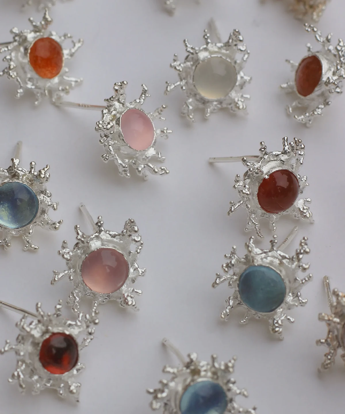 Gemstone Stud Earrings in S925 Sterling Silver with organic splash-inspired silverwork and smooth cabochon-cut stones in pink, blue, red, orange, and white; arranged on flat surface to showcase artisanal variety and vibrant elegance.