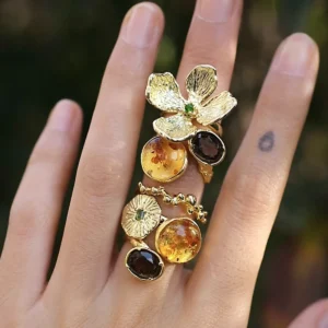 Gold Plated S925 Sterling Silver Amber Ring with Dual Gemstones 07 Hand wearing an ornate gold toned Amber Ring with multiple amber stones, dark gemstones, and floral details spanning two fingers.