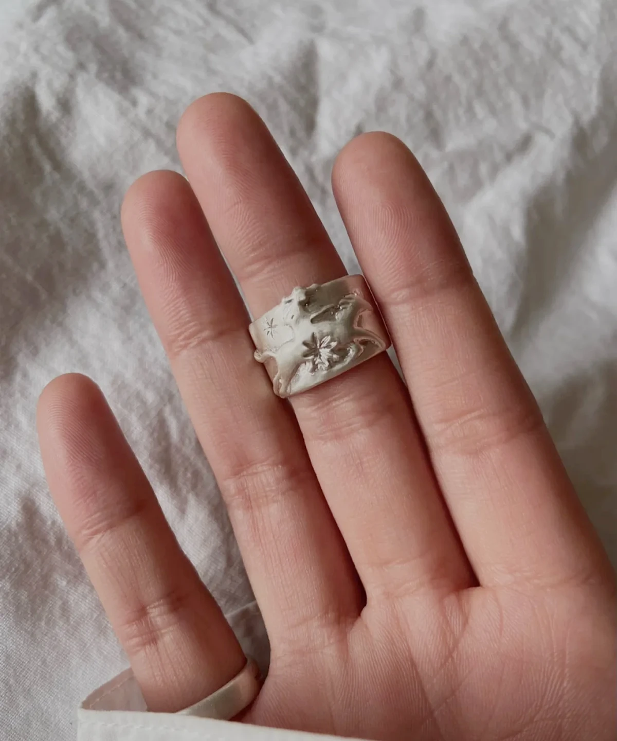 Handcrafted 999 Silver Ring with cowboy and horse motif; worn on middle finger over soft white fabric, featuring star and floral engravings that highlight poetic detail and artisan Horse Ring craftsmanship.