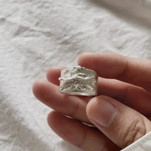 Handcrafted 999 Silver Ring with embossed cowboy and horse motif; held in hand over soft white fabric, showcasing intricate floral engravings and textured band design. A poetic Horse Ring blending western spirit with artisan silverwork.