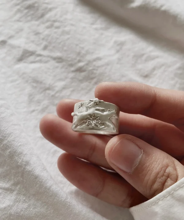 New In 33 Handcrafted 999 Silver Ring with embossed cowboy and horse motif; held in hand over soft white fabric, showcasing intricate floral engravings and textured band design. A poetic Horse Ring blending western spirit with artisan silverwork.