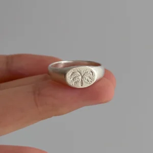 999 Silver Signet Ring with engraved palm tree design featuring textured fronds and trunk; handcrafted Silver Signet Ring held between fingers, styled against neutral background to highlight artisanal detail.