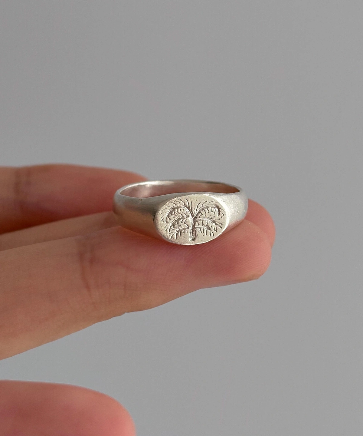 999 Silver Signet Ring with engraved palm tree design featuring textured fronds and trunk; handcrafted Silver Signet Ring held between fingers, styled against neutral background to highlight artisanal detail.