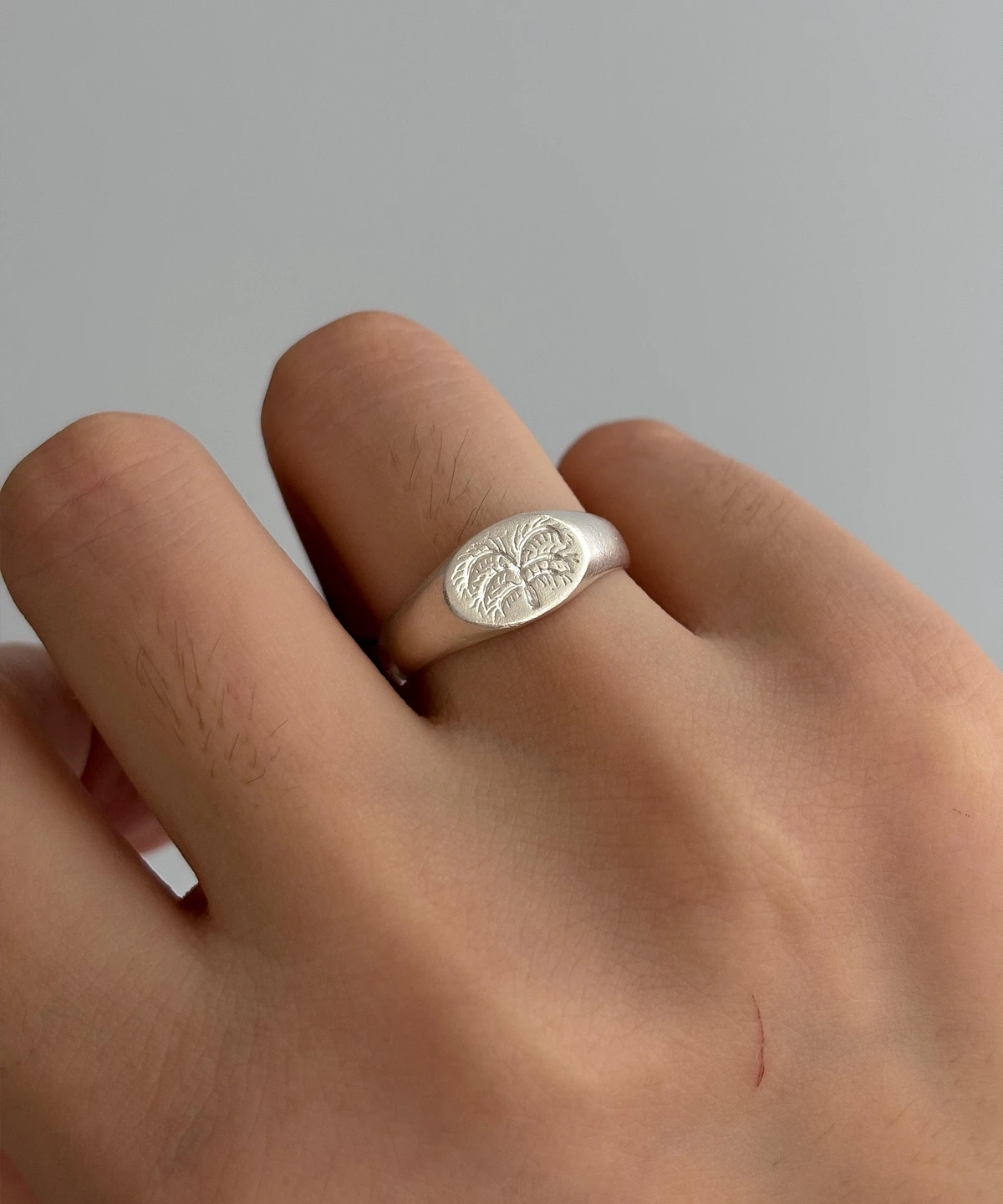 999 Silver Signet Ring with engraved twin palm tree design on oval face; handcrafted Silver Signet Ring worn on middle finger, styled against neutral background to highlight organic detailing and artisanal craftsmanship.