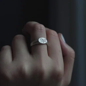 999 Silver Signet Ring with engraved butterfly motif on circular face; handcrafted Silver Signet Ring worn on middle finger, styled in dim lighting against dark background to highlight intricate detail and organic elegance.